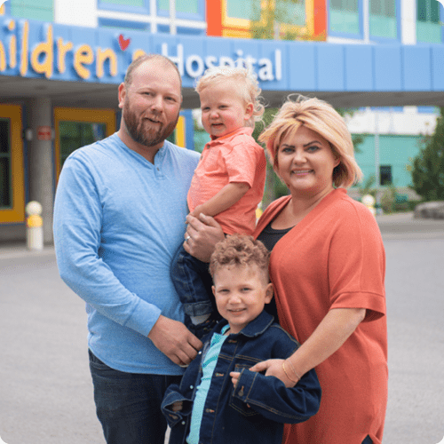 Leo with mom, dad and brother in front of the Alberta Children's Hospital
